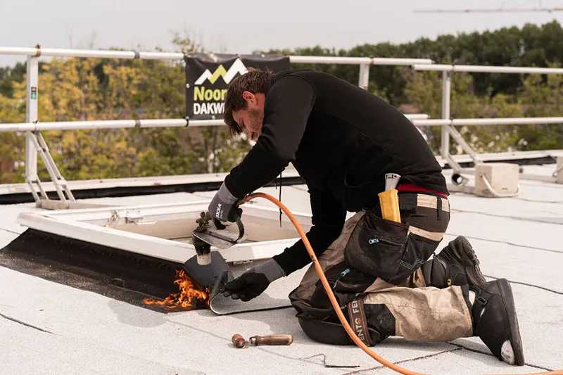 Dakdekker brandt bitumen dakbedekking bij een dakraam op een plat dak in Haarlem