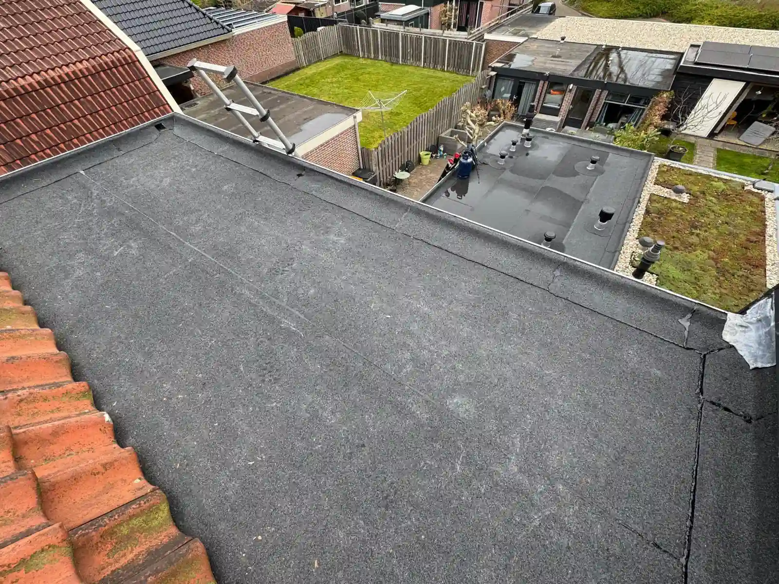 Nieuw bitumen plat dak van een uitbouw in Heerhugowaard, met de aansluiting op het rode pannendak, uitgevoerd door NH Dakwerken
