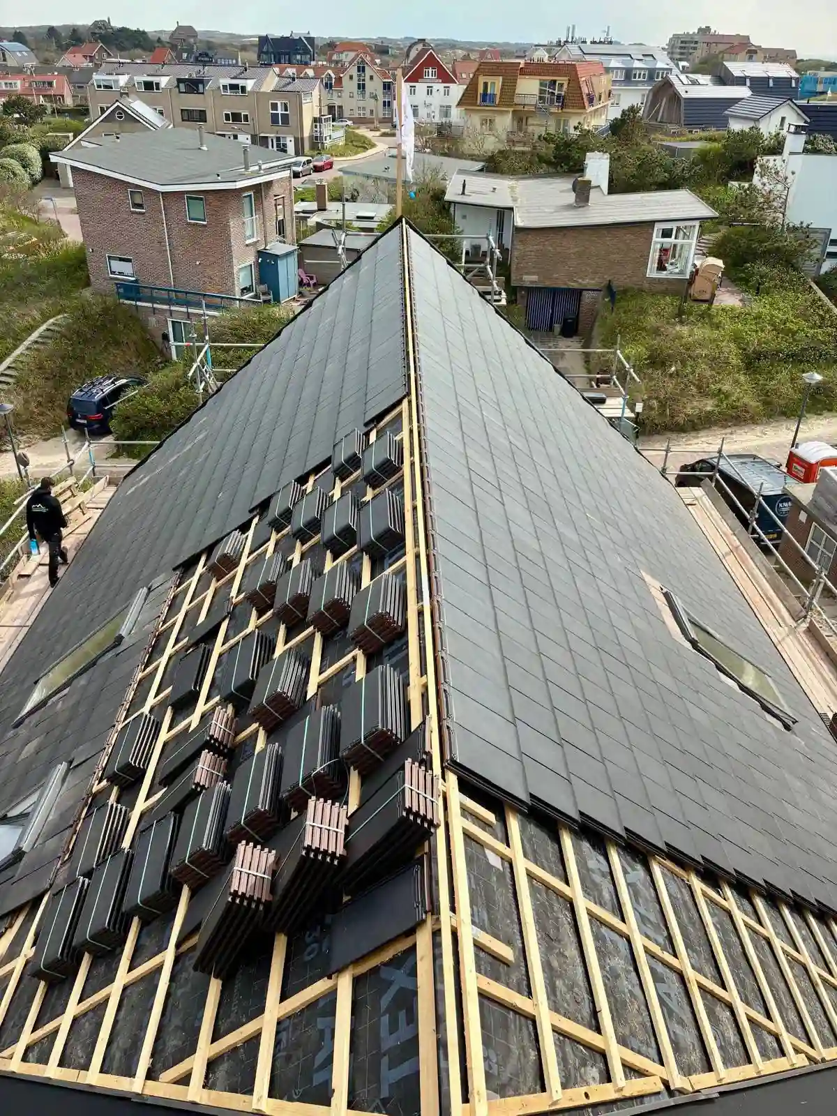 Luchtfoto van het deels gedekte dakvlak met zwarte Monier Tuile vlakke dakpannen en dakramen in Bergen aan Zee