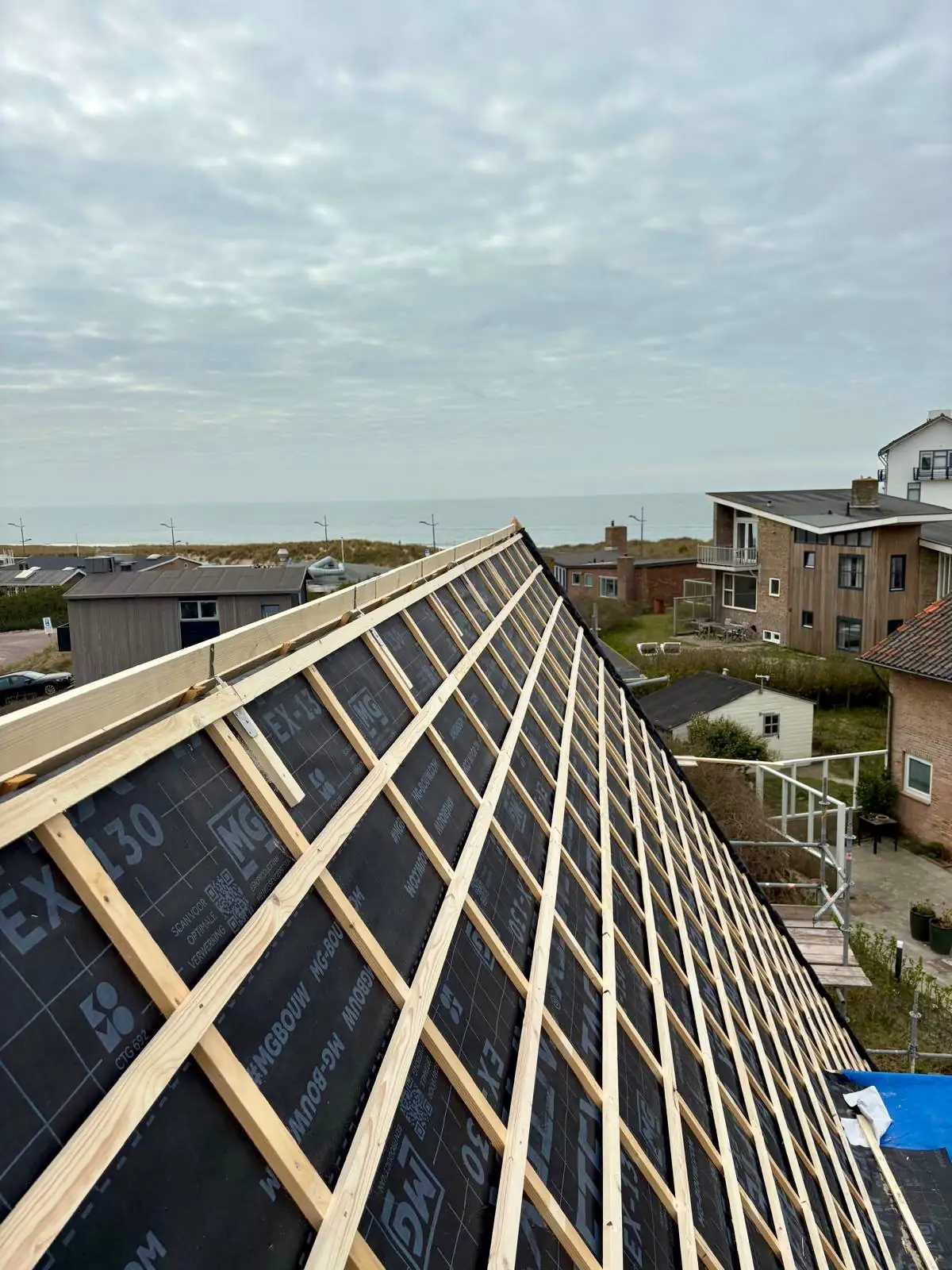 Dampopen onderdakfolie met tengels en nieuwe panlatten op het dak, gezien vanaf de nok met de zee op de achtergrond in Bergen aan Zee