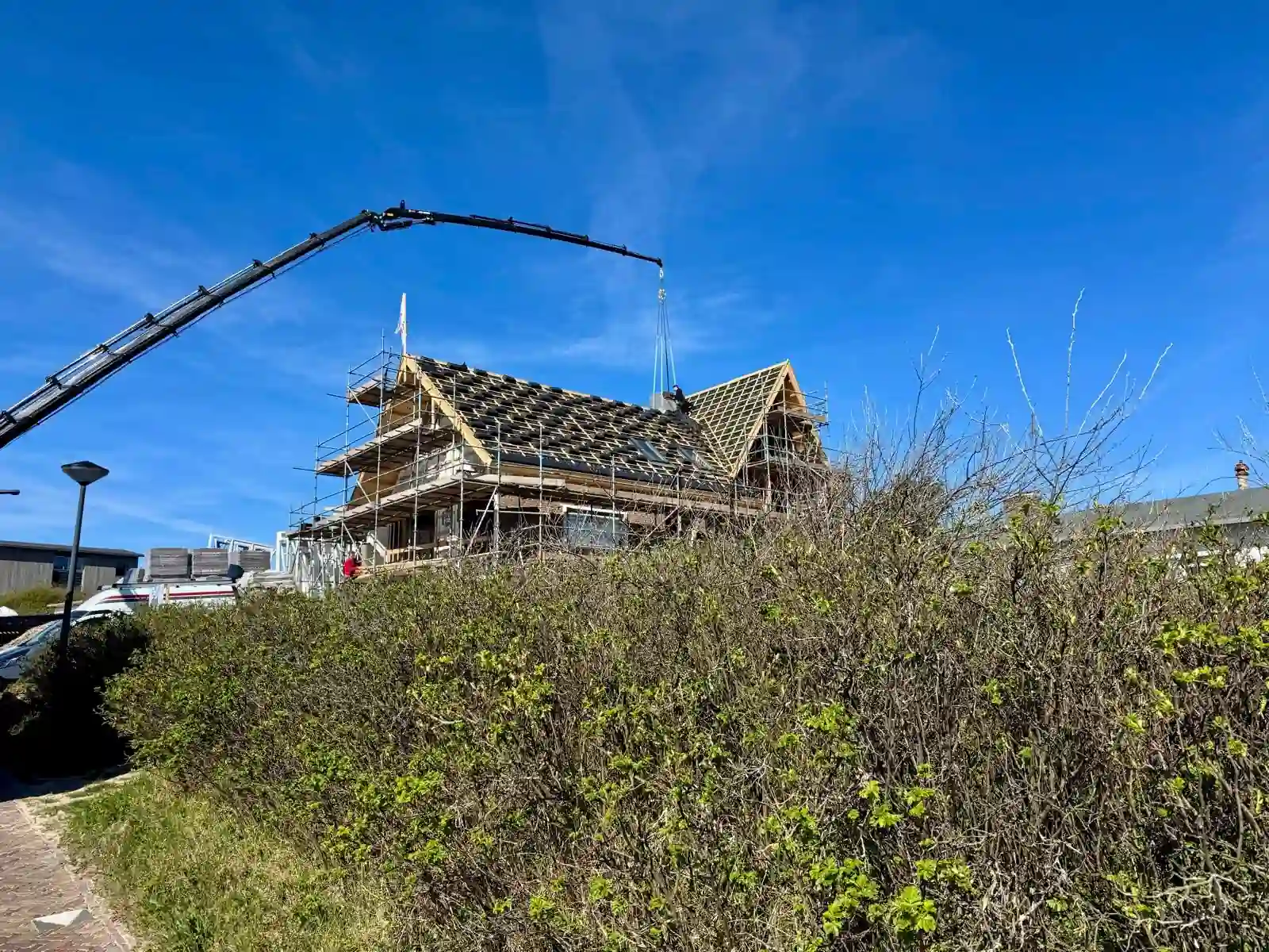 Hijskraan zet pakketten zwarte dakpannen op het dak van een woning in Bergen aan Zee tijdens de pannendak renovatie door NH Dakwerken